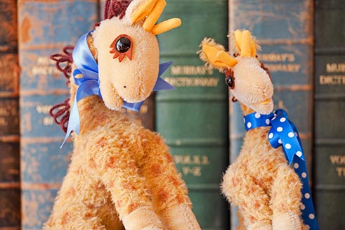 Two heirloom, hand-crafted giraffes, in front of a row of antique books. 