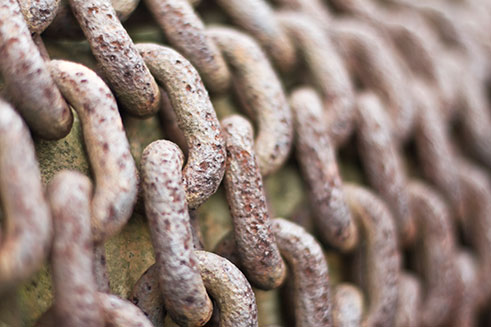 A close-up image of several lengths of heavy metal chain, rusty with age. 